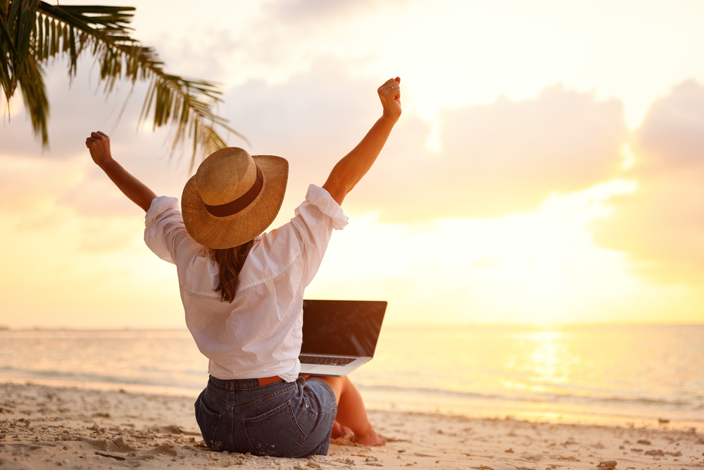 Contract to Hire Jobs: a remote worker with her laptop sitting at the edge of the beach